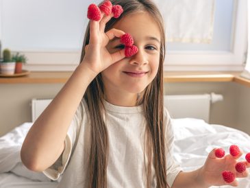 Funny little girl with raspberries on her fingers in bed in the morning